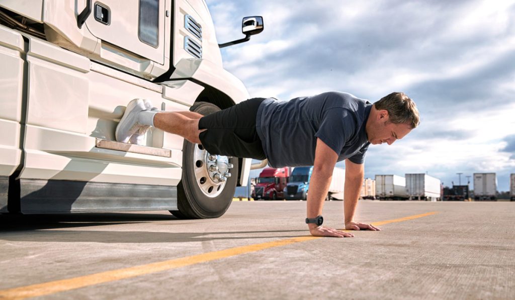 A man doing push ups in front of a truck.